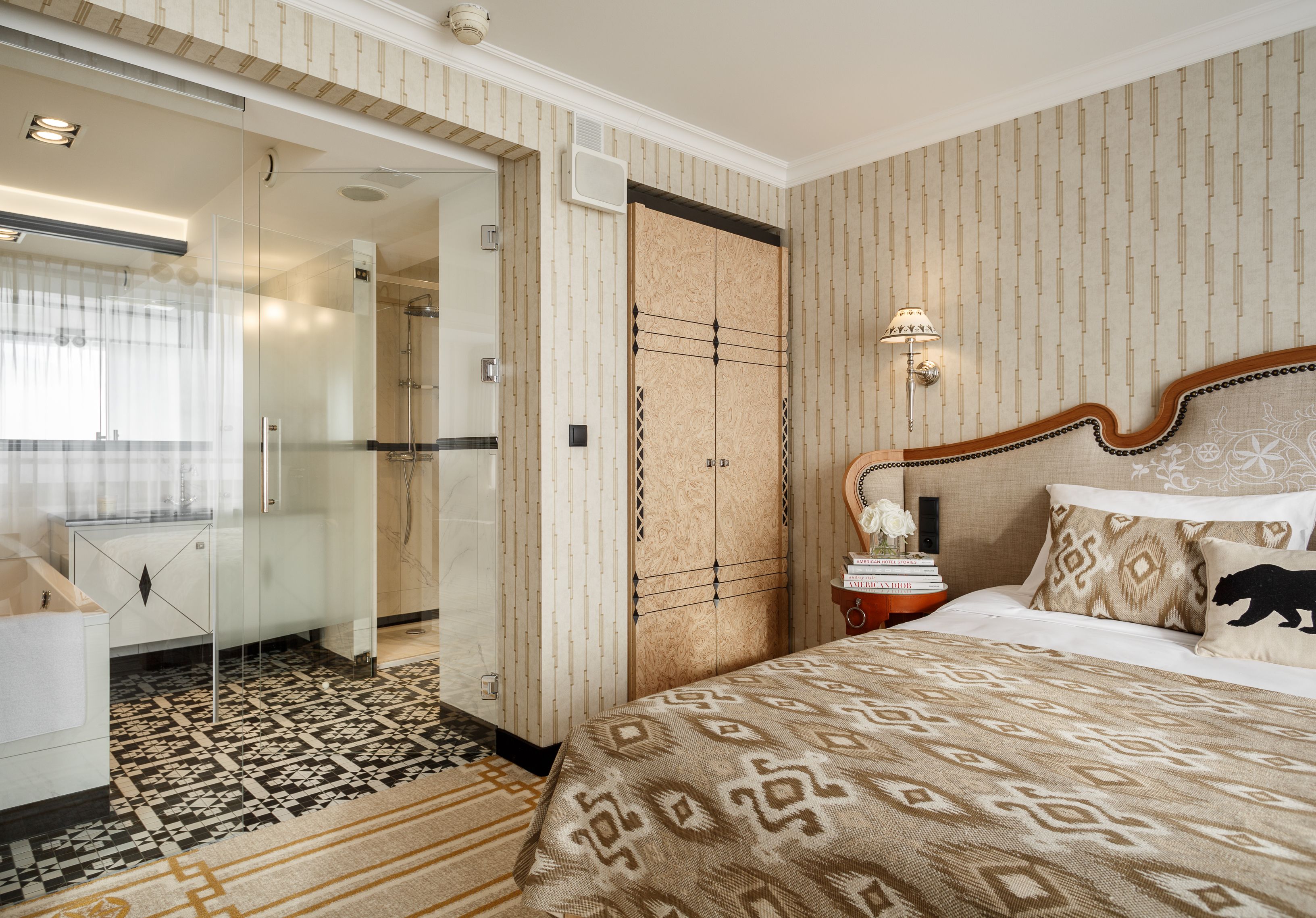 A hotel room with a large bed, a glass shower enclosure, a patterned carpet, and a wardrobe with a unique design.