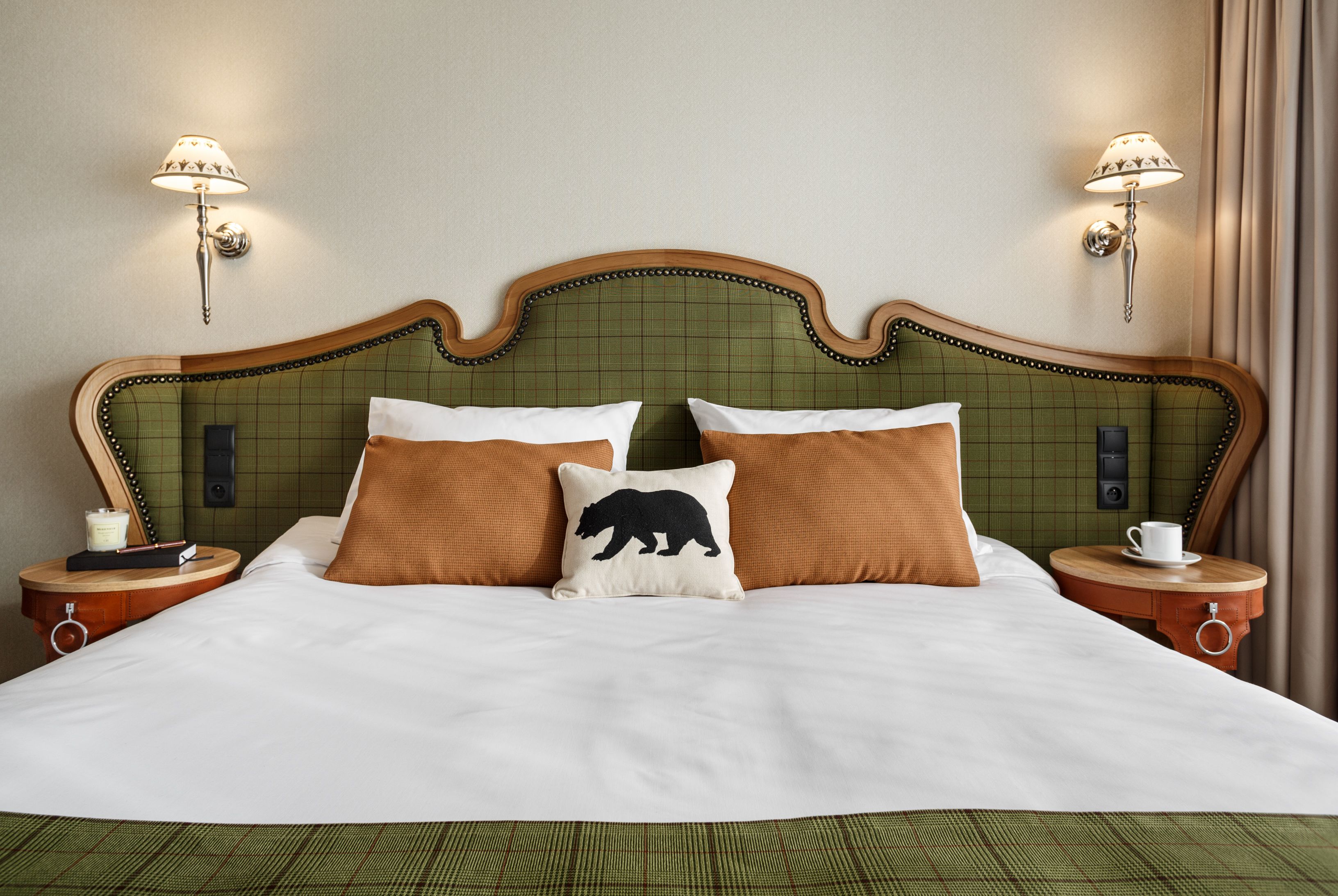 A neatly made bed with a green headboard, two bedside tables with lamps, and a pillow with a bear design.