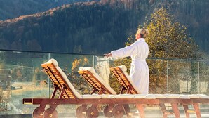 A person in a white robe standing by a pool with lounge chairs, overlooking a mountainous landscape.