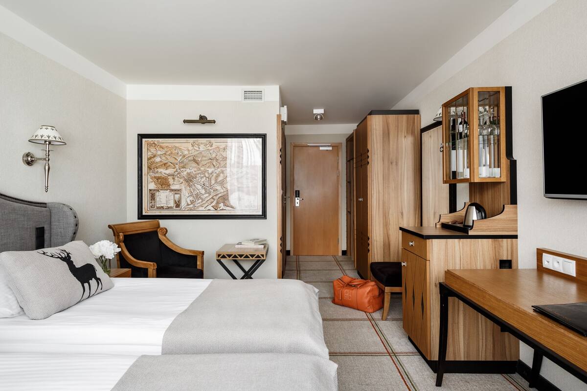 A hotel room with a bed, a desk, a chair, a wardrobe, and a television.