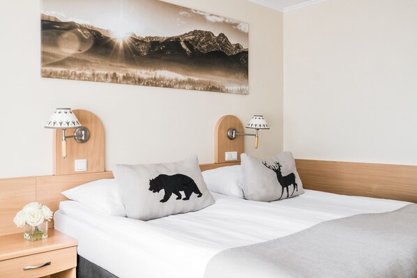 A neatly made bed with two pillows, a nightstand with a lamp, and a wall-mounted picture of a mountain landscape. - Bachleda Hotel Kasprowy**** (Zakopane)