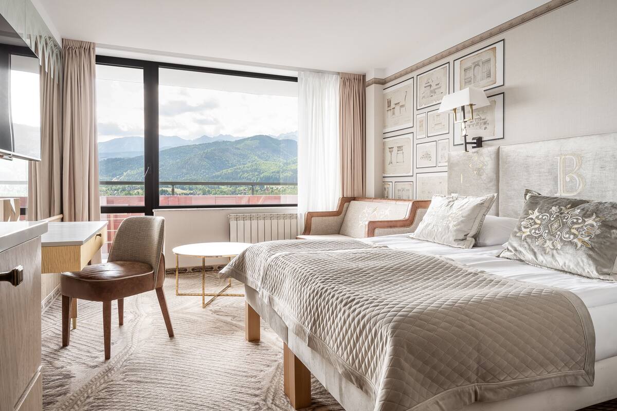 A hotel room with a large bed, a desk, a chair, and a view of mountains.