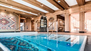 A swimming pool with a mosaic tile design, wooden beams, and a staircase leading to an upper level.