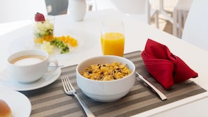 Desayuno con un tazón de cereal, un vaso de jugo de naranja y una taza de café sobre una mesa blanca.
