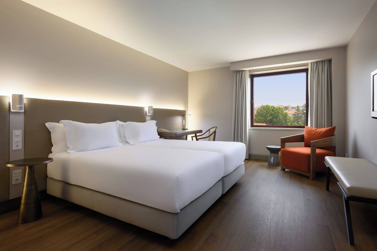 Habitación de hotel con una cama grande, un escritorio, una silla y vistas al exterior.
