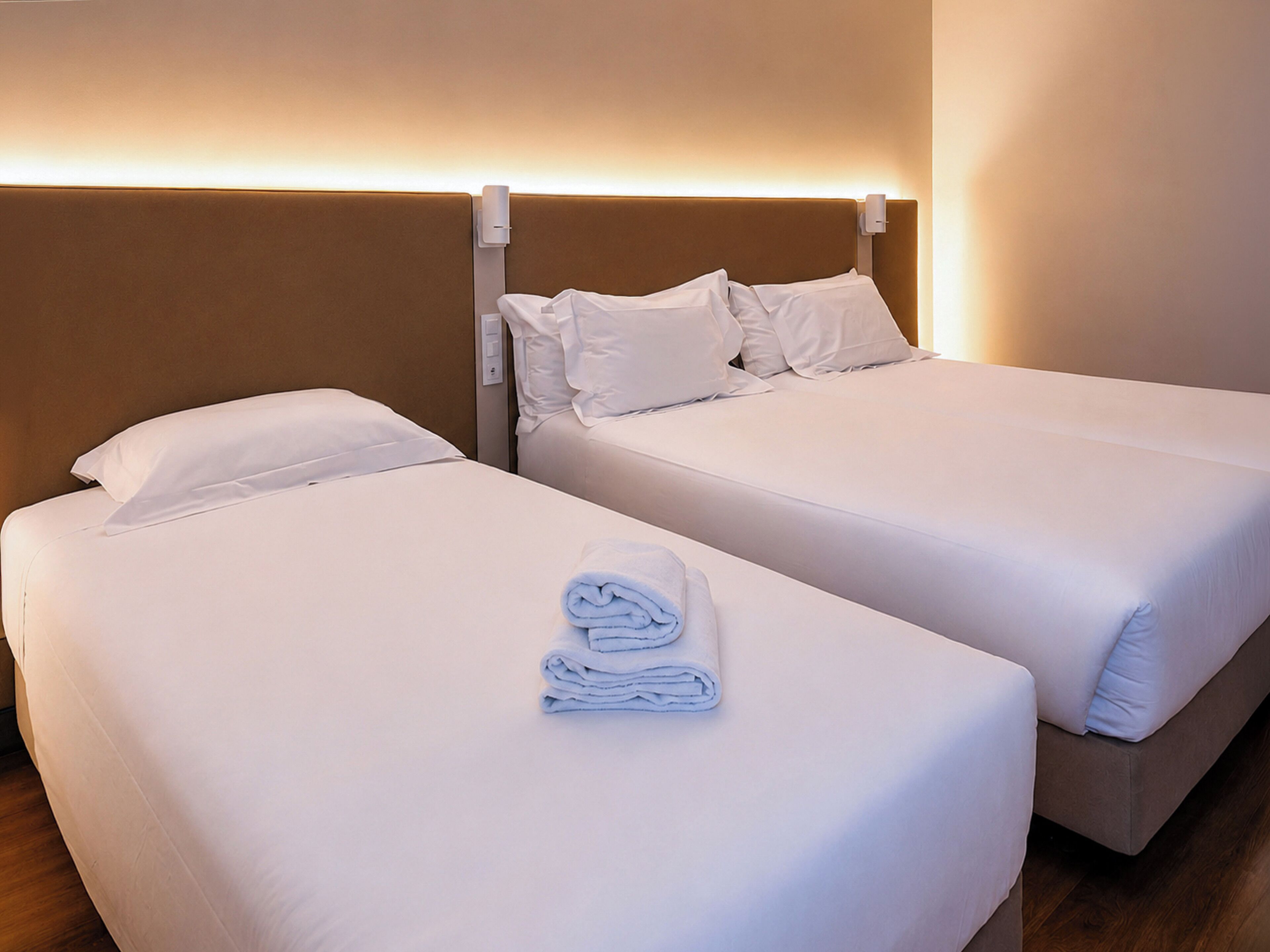 A hotel room with two beds, each with white linens and pillows, and a neatly folded towel on the left bed.