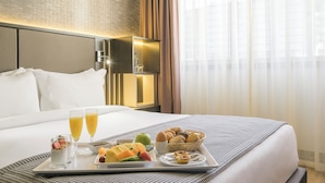 A hotel room with a neatly made bed, a tray with breakfast including fruits, pastries, and juice, and a large window with curtains. - HF Fénix Lisboa (Lisbon)