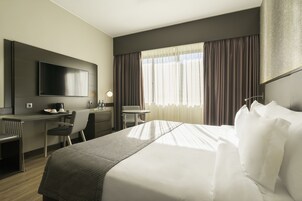 Une chambre d’hôtel équipée d’un lit, d’un bureau, d’une chaise, d’une télévision et de rideaux.