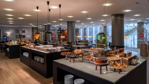 A modern hotel lobby with a buffet area featuring various food items and a seating area with tables and chairs. - HF Fénix Lisboa (Lisbon)