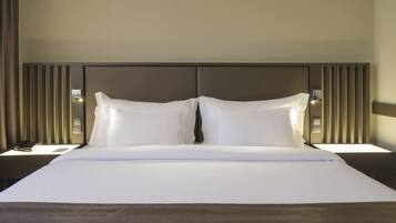 Quarto de hotel com uma cama grande, duas mesas de cabeceira e uma cabeceira moderna.