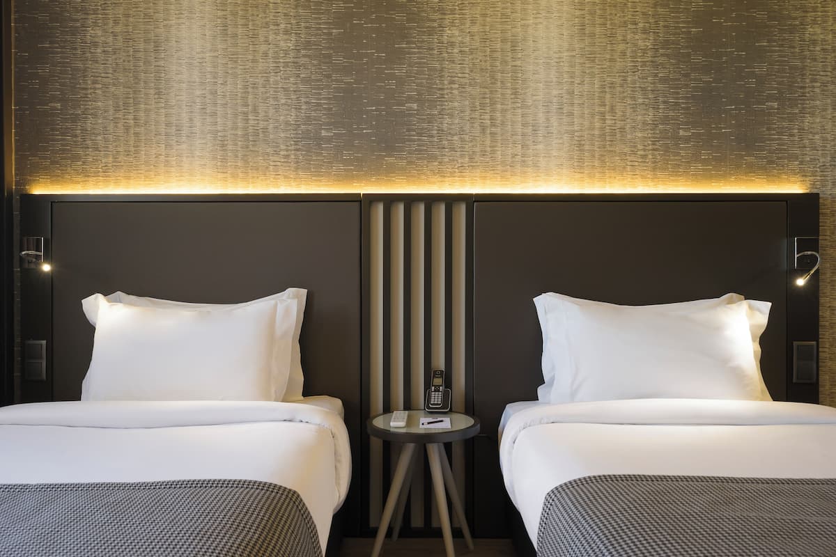 Ein Hotelzimmer mit zwei Betten, einem kleinen Tisch mit Telefon und einer strukturierten Wand.