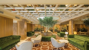 A lobby with green sofas, a central tree, and a geometric patterned floor. - HF Fénix Lisboa (Lisbon)
