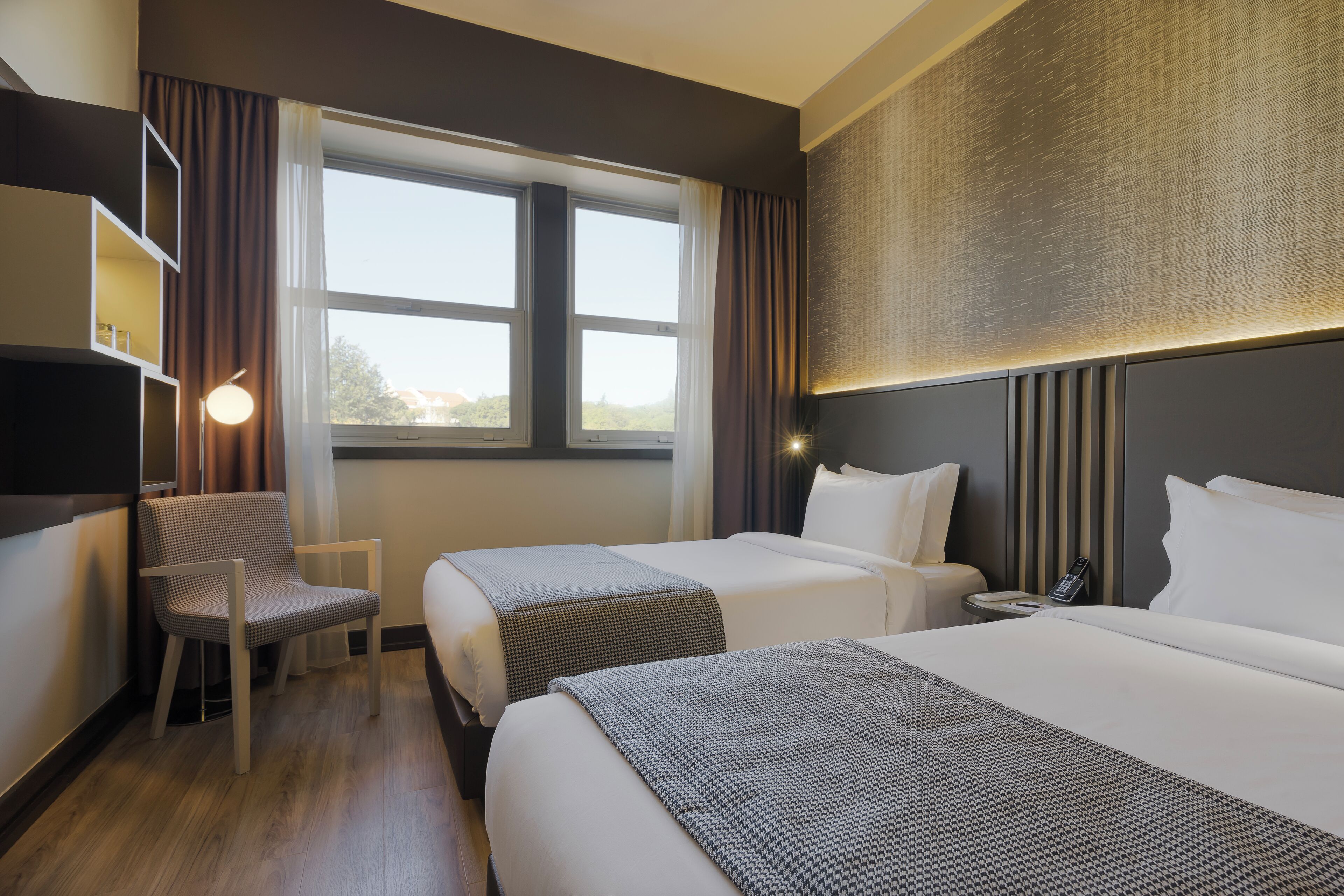 Une chambre d’hôtel avec deux lits, un bureau, une chaise, une télévision et une fenêtre avec des rideaux.