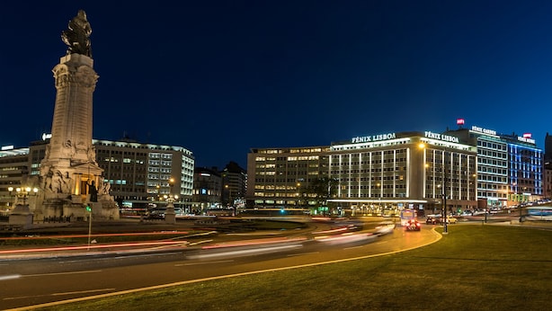 A nighttime cityscape with a prominent monument, modern buildings, and a well-lit intersection. - HF Fénix Lisboa (Lisbon)