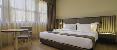 Ein modernes Hotelzimmer mit einem großen Bett, einem Nachttisch, einem Sessel und einem kleinen runden Tisch.