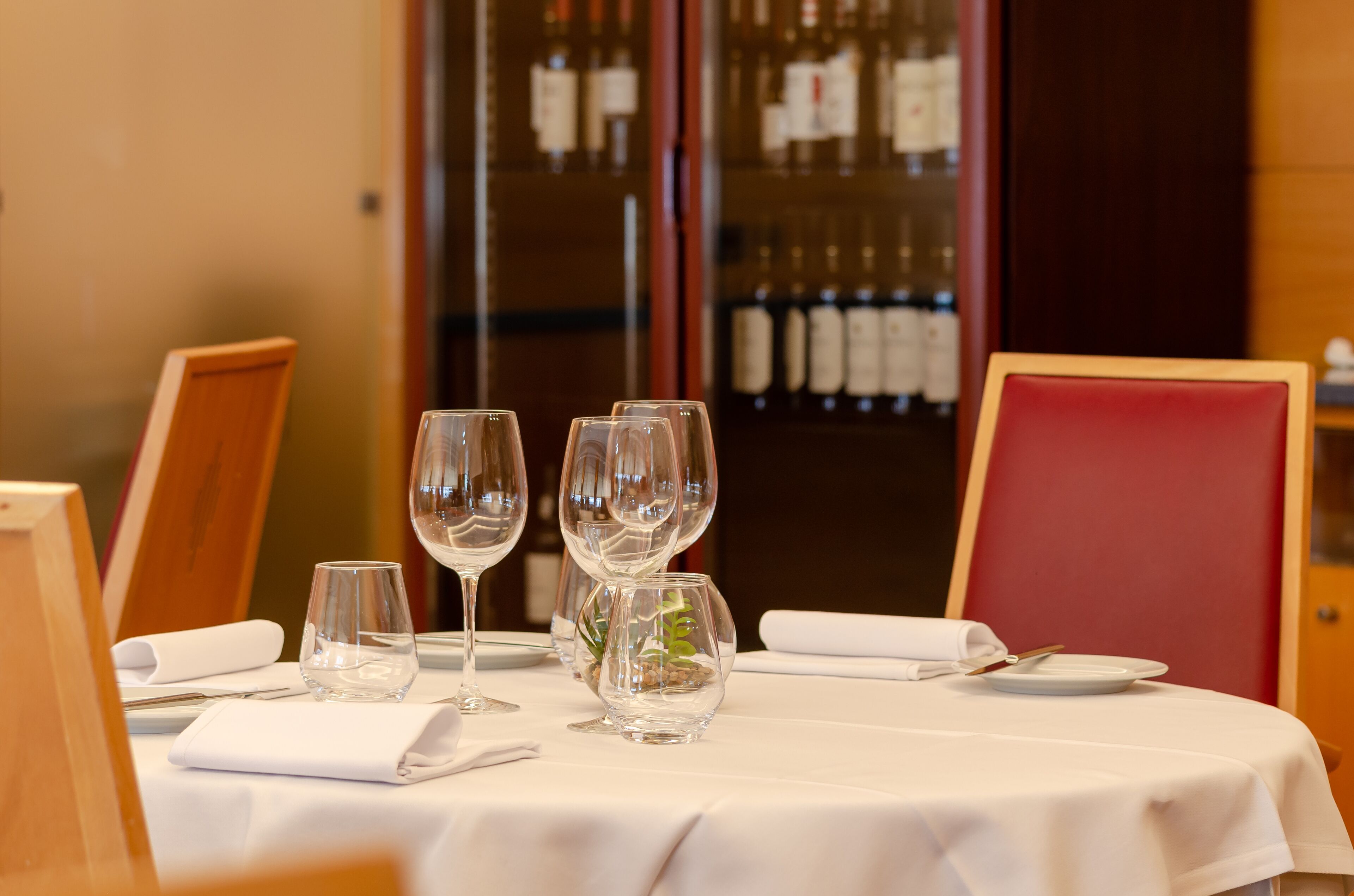 Una mesa de comedor dispuesta con copas de vino, una copa pequeña, un plato y una servilleta.
