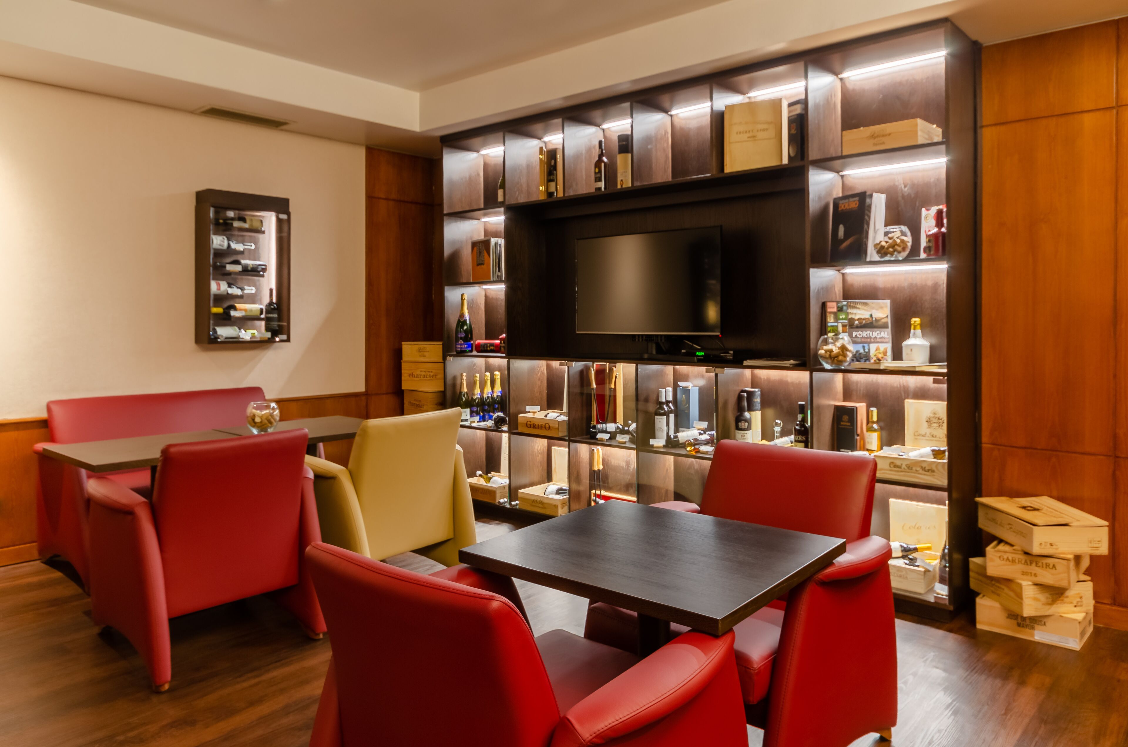 Habitación de hotel con un mueble de madera que exhibe varios objetos, un televisor de pantalla plana y asientos tapizados en rojo.