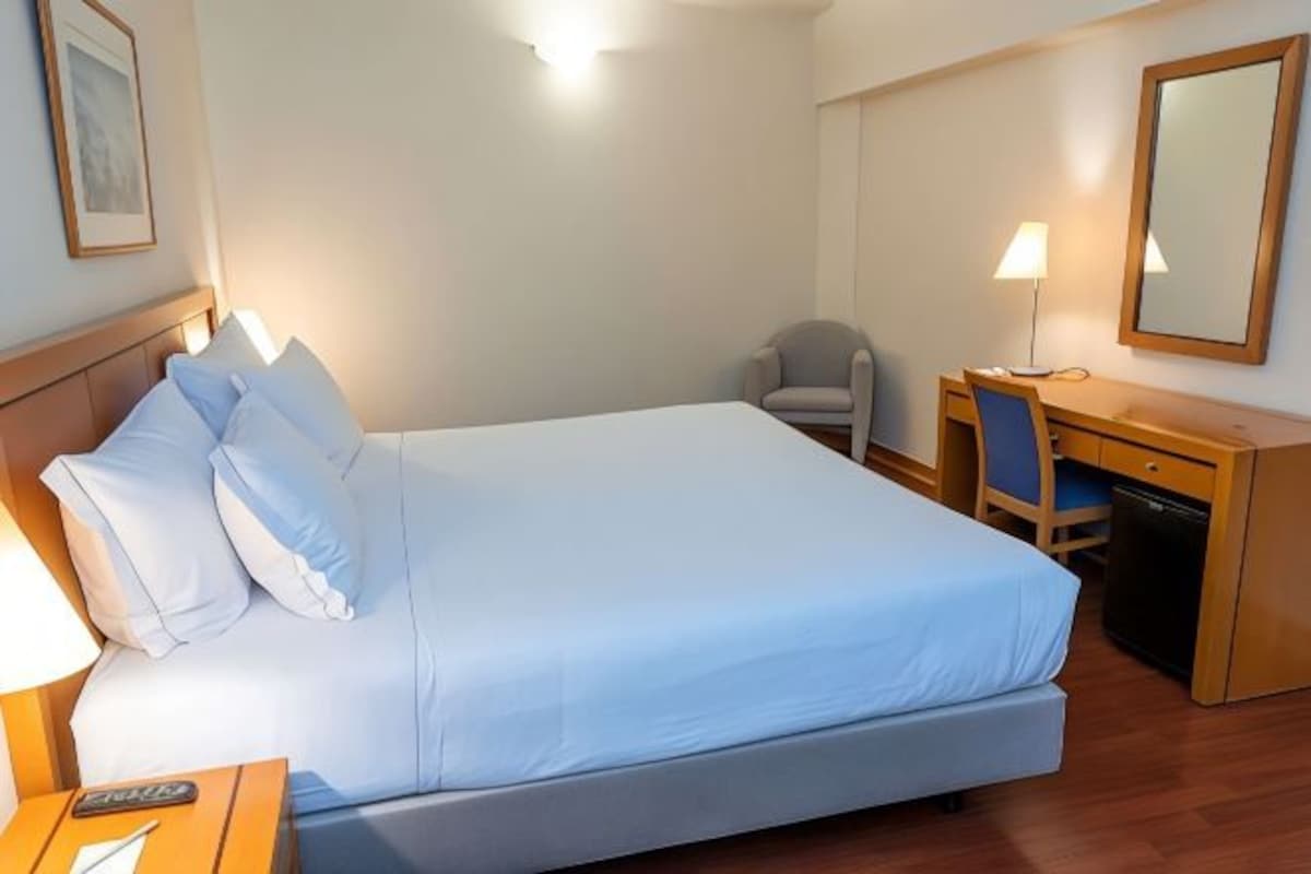 A hotel room with a bed, a desk, a chair, a lamp, and a small cabinet.