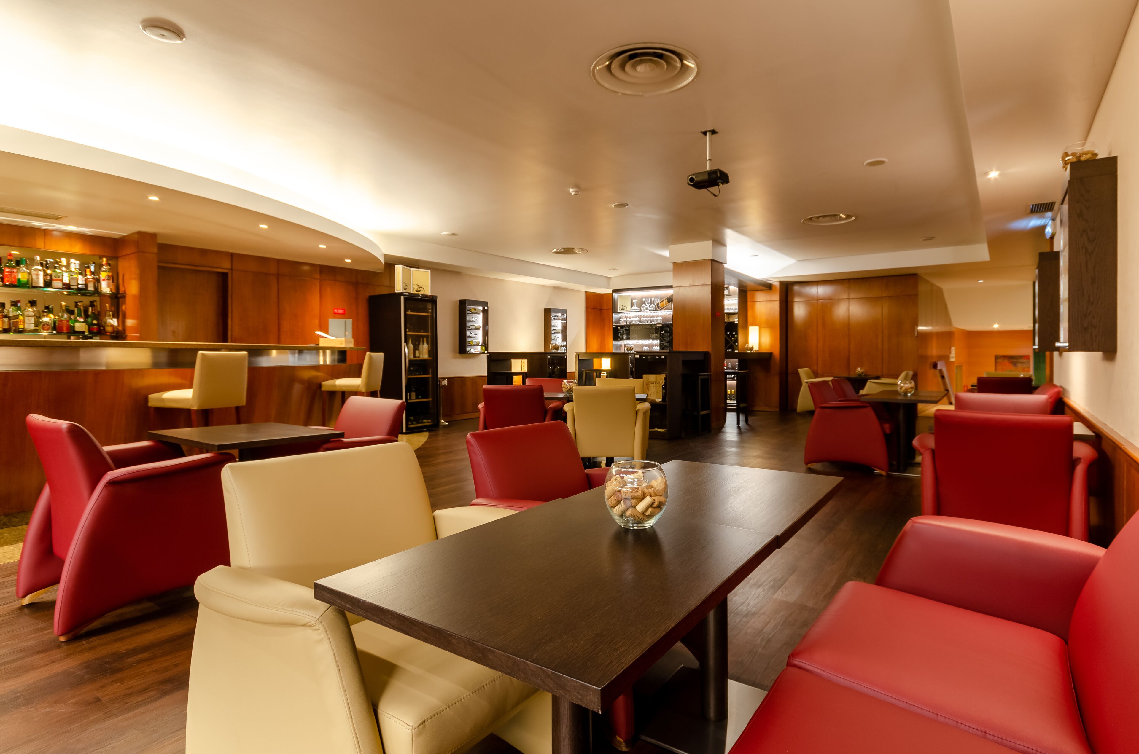 A modern hotel lobby with a bar area, leather seating, and a wooden reception desk.