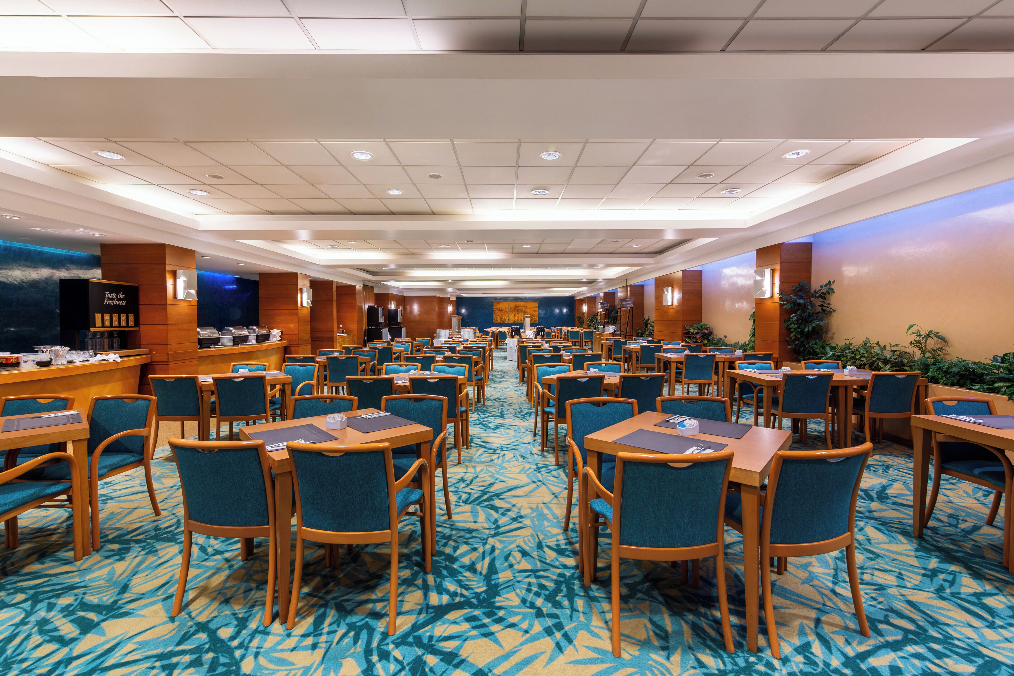 Un salón de conferencias de hotel con filas de mesas y sillas, un mostrador de recepción y una pantalla grande.