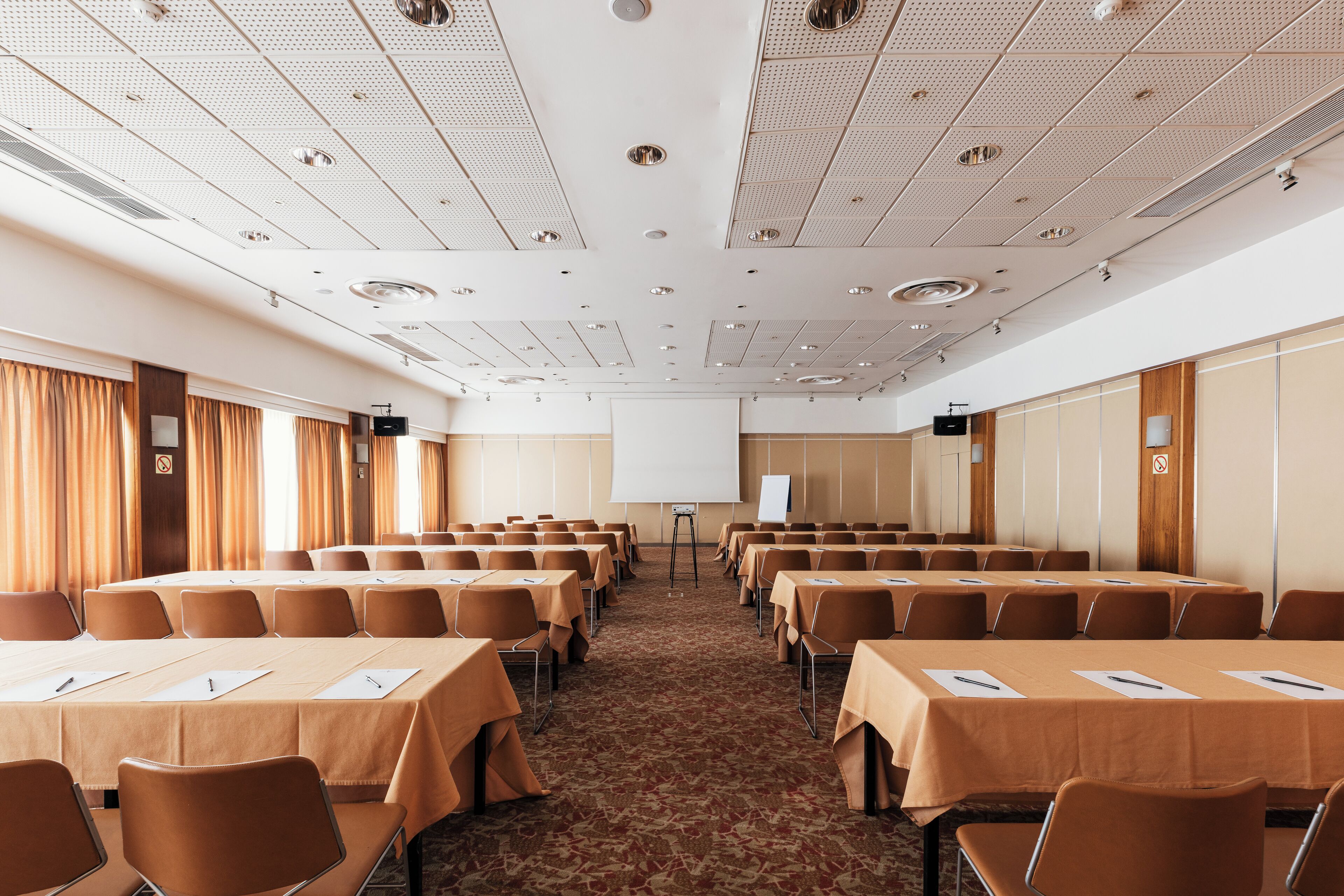 Une salle de conférence avec des rangées de tables et de chaises, un tableau blanc et un écran de projection.
