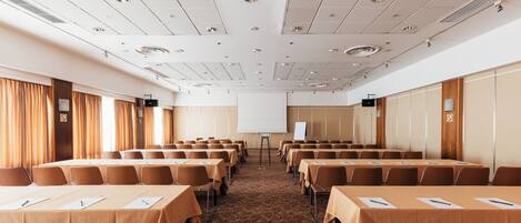 A conference room with rows of tables and chairs, a whiteboard, and a projector screen.