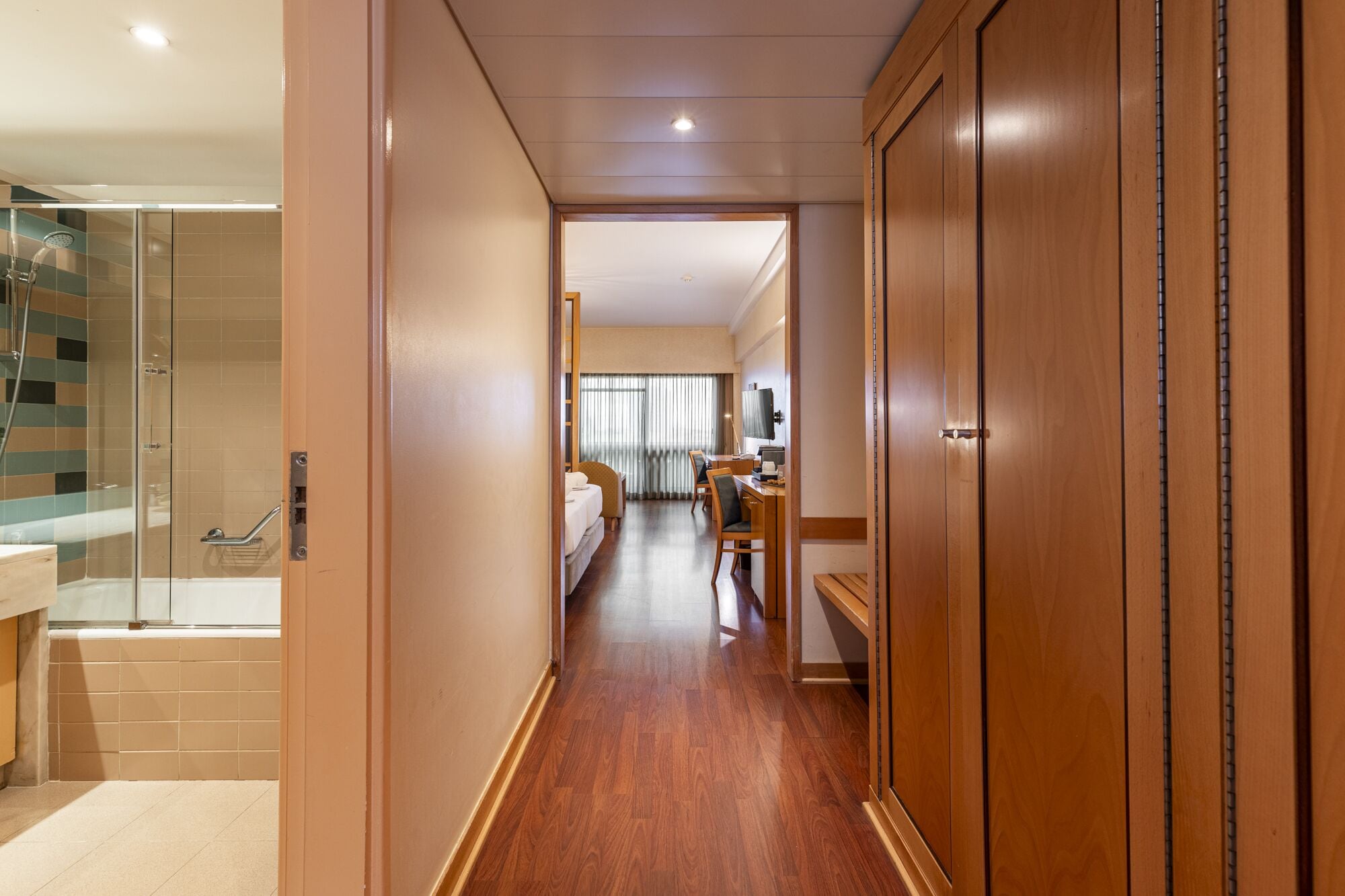 A hotel hallway with a shower, a bed, a desk, and a TV.
