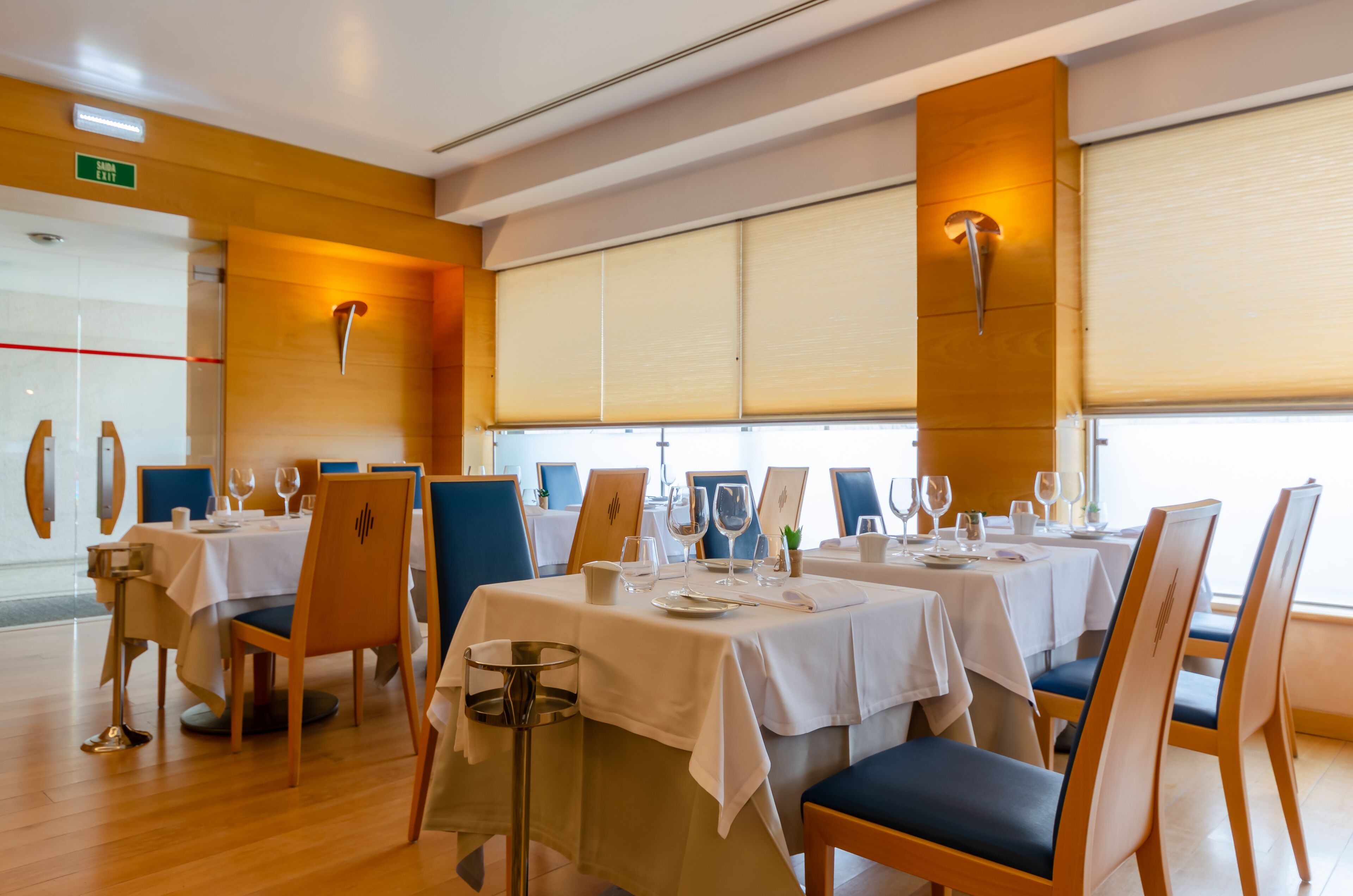 A restaurant with tables set for dining, chairs, and a window with blinds.