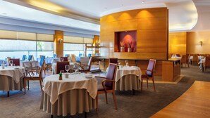 A modern restaurant with round tables and chairs, a wooden accent wall, and a view of the outdoors.