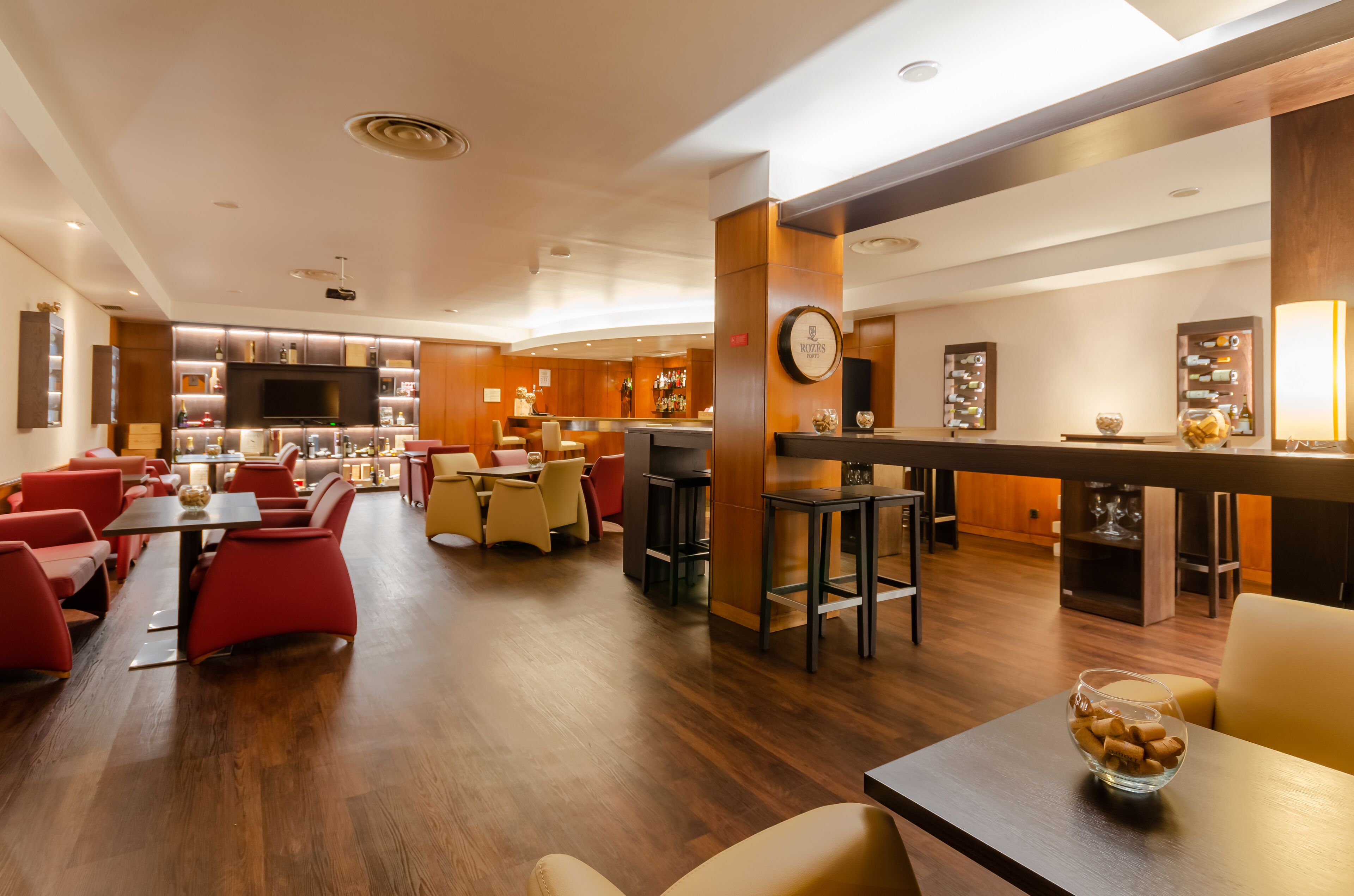 Un vestíbulo de hotel con una zona de bar, arreglos de asientos y una pantalla de televisión.