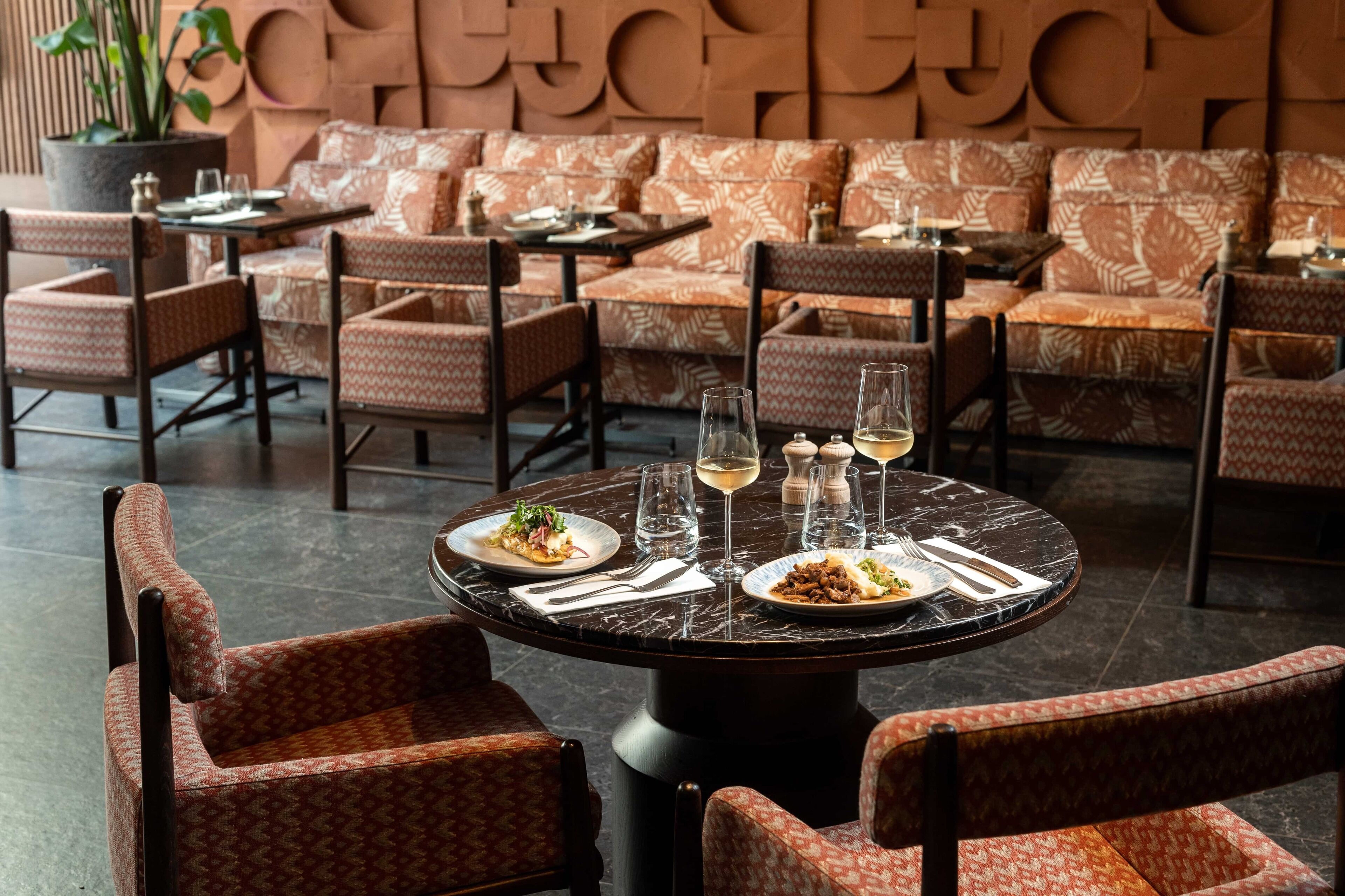Un restaurant avec des tables rondes, des chaises à motifs et un mur orné de dessins géométriques.