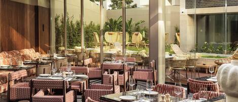 Un restaurante con mesas y sillas, un ventanal grande y vistas al exterior.
