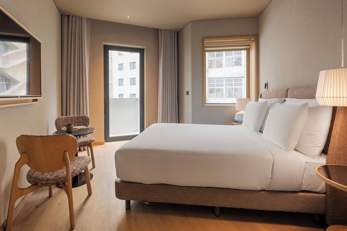 A hotel room with a large bed, a chair, a table, and a window with curtains.