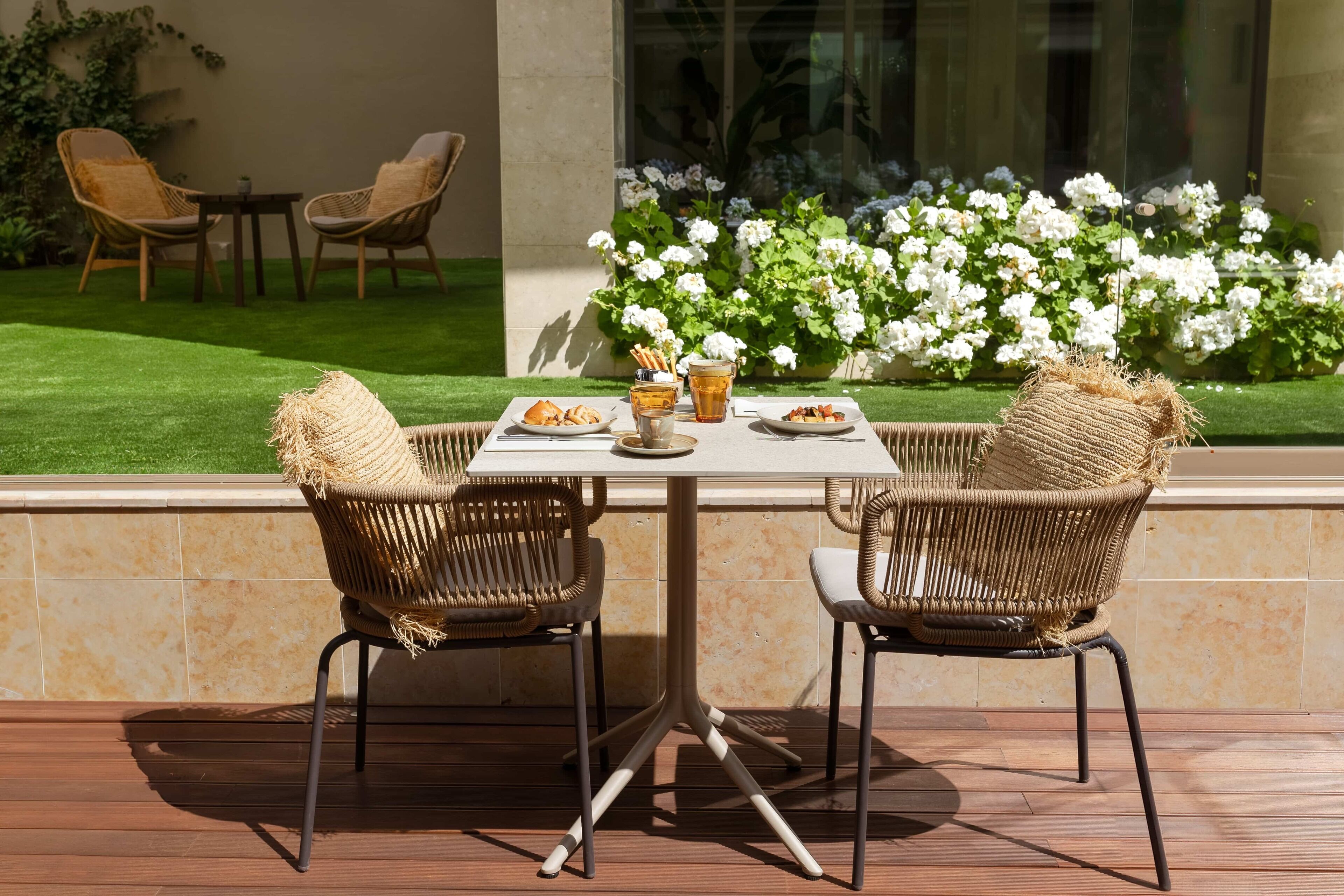 Une terrasse extérieure avec deux fauteuils en osier, une table et un verre contenant une boisson.