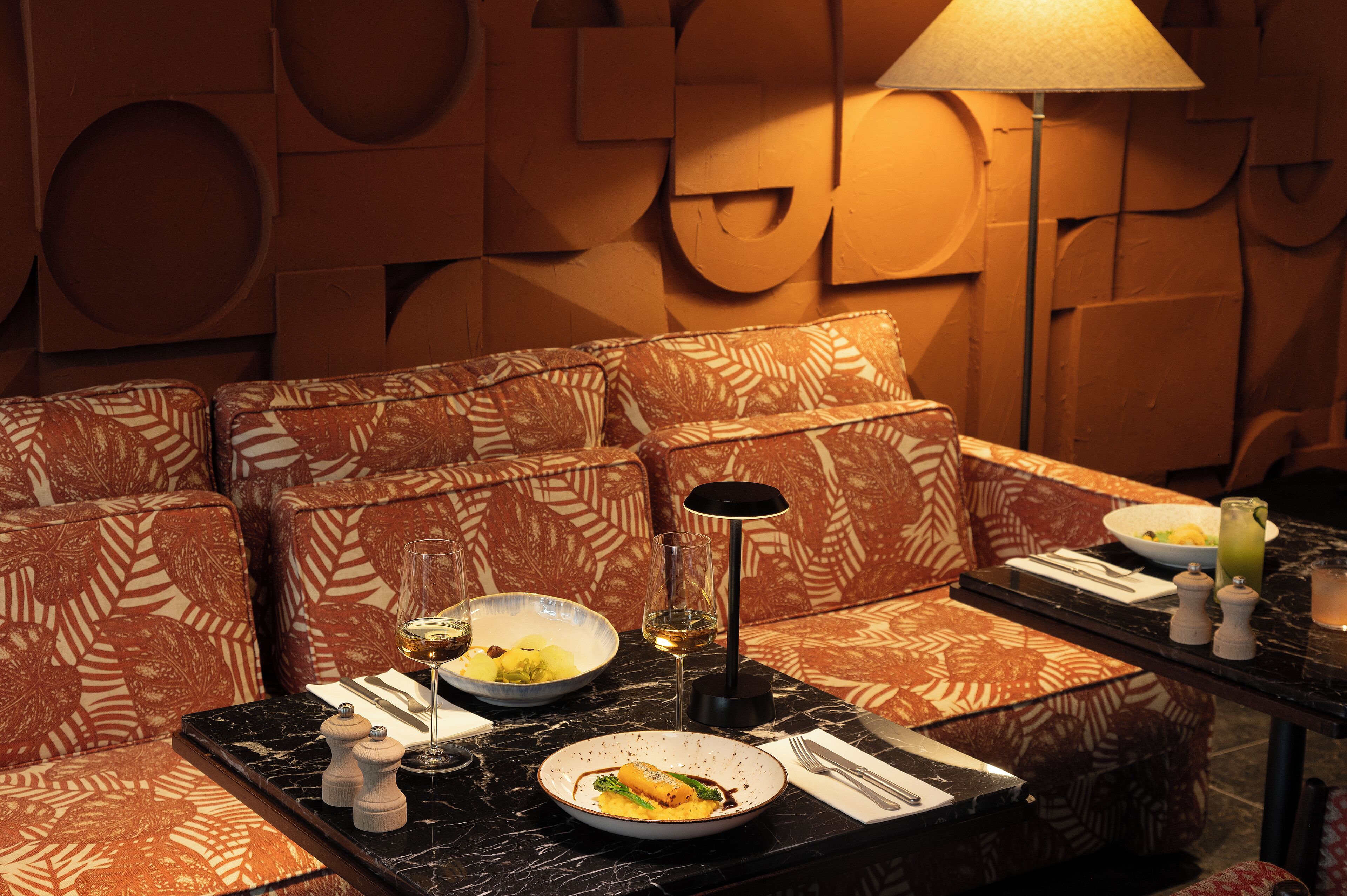 A dining area with patterned sofas, a table set with plates, glasses, and a lamp.