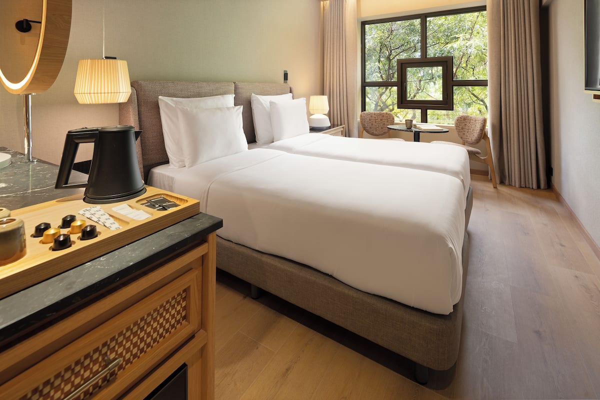 A hotel room with a large bed, a desk with a coffee maker, a chair, and a window with curtains.