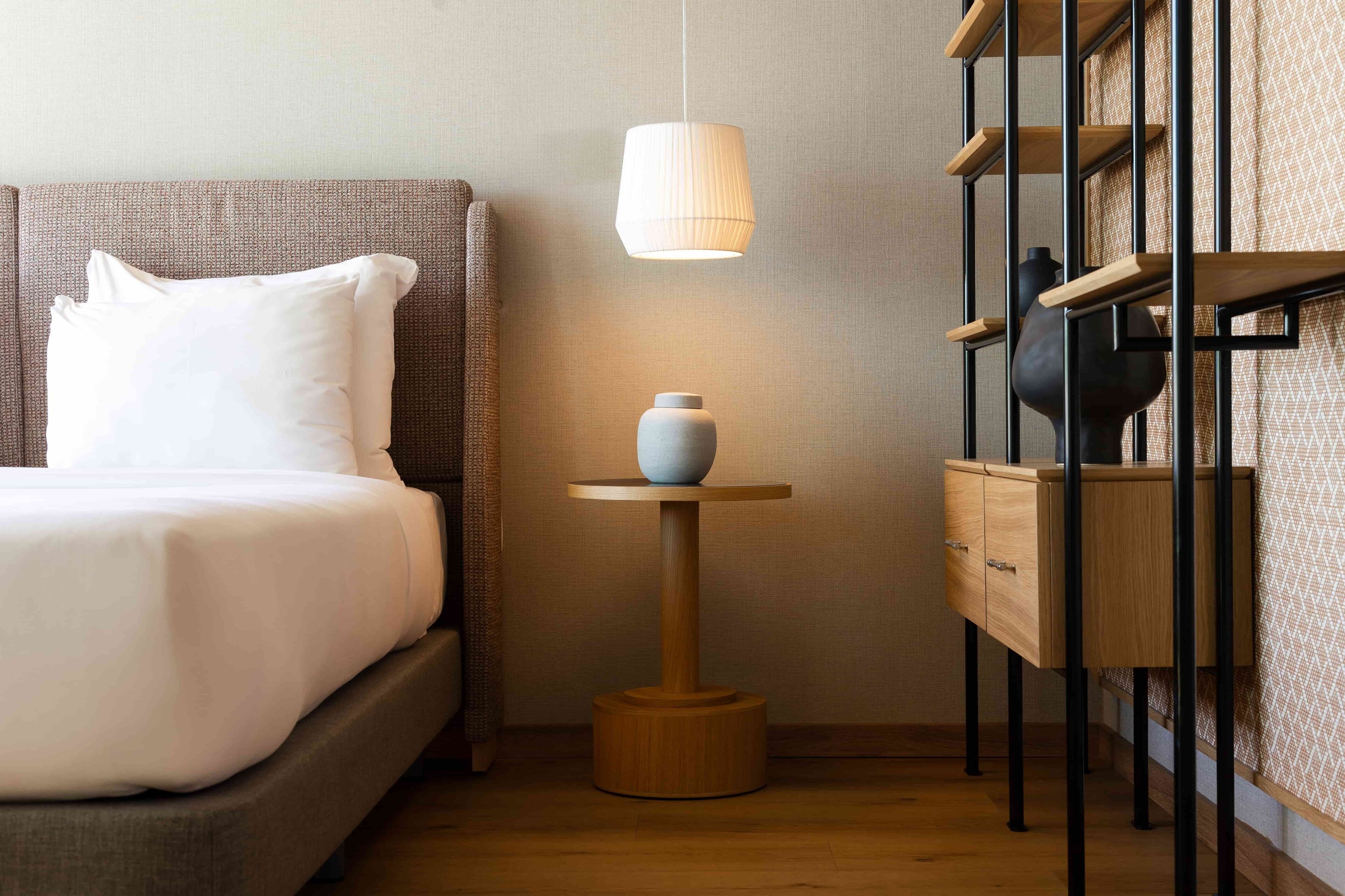 Habitación de hotel ordenada con una cama, una mesita de noche con lámpara y un mueble pequeño.