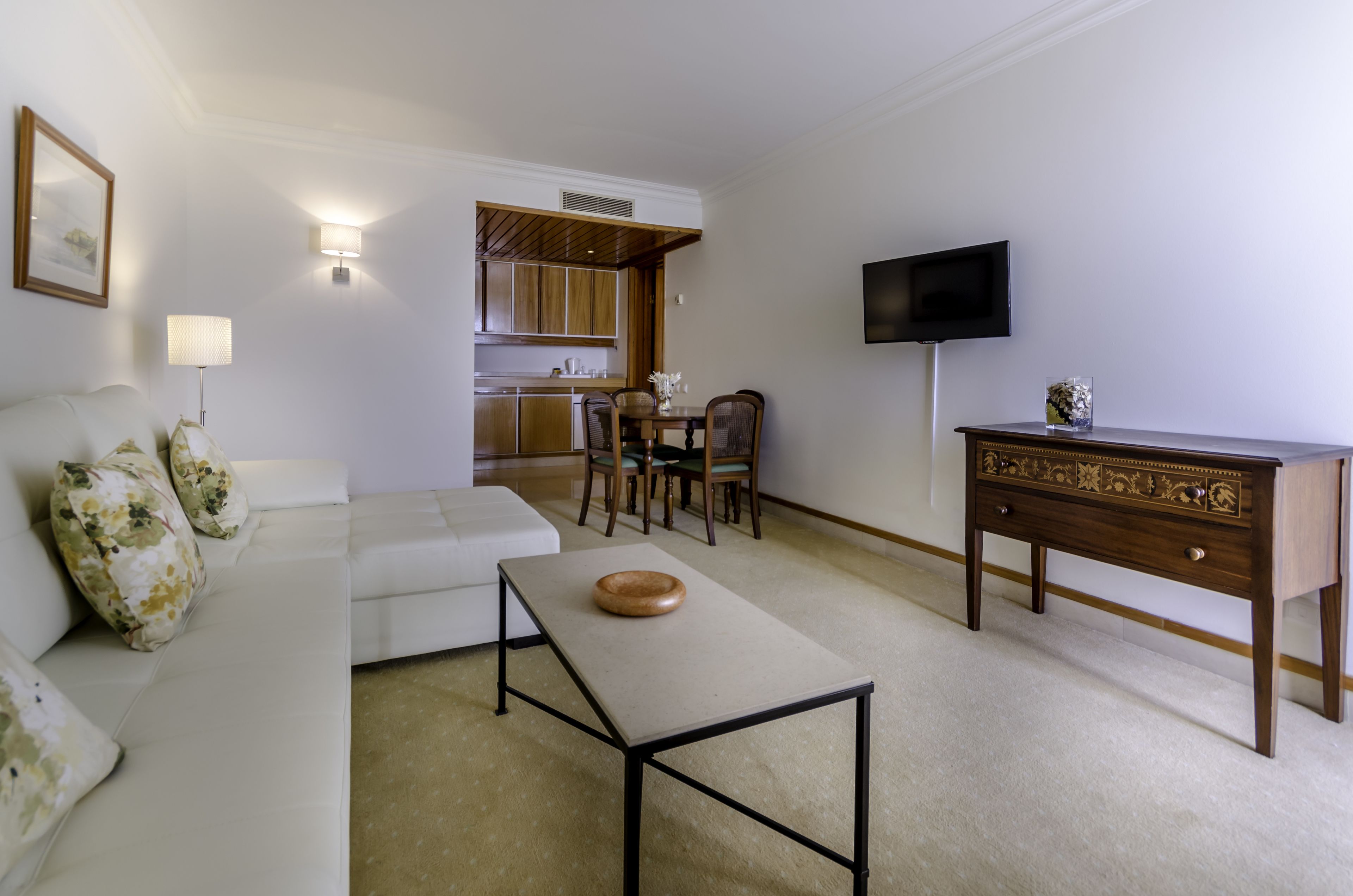 A living room with a white sofa, a coffee table, a wooden side table, and a TV on the wall.