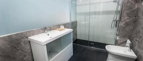 A modern bathroom with a glass-enclosed shower, a white vanity, and a separate toilet.