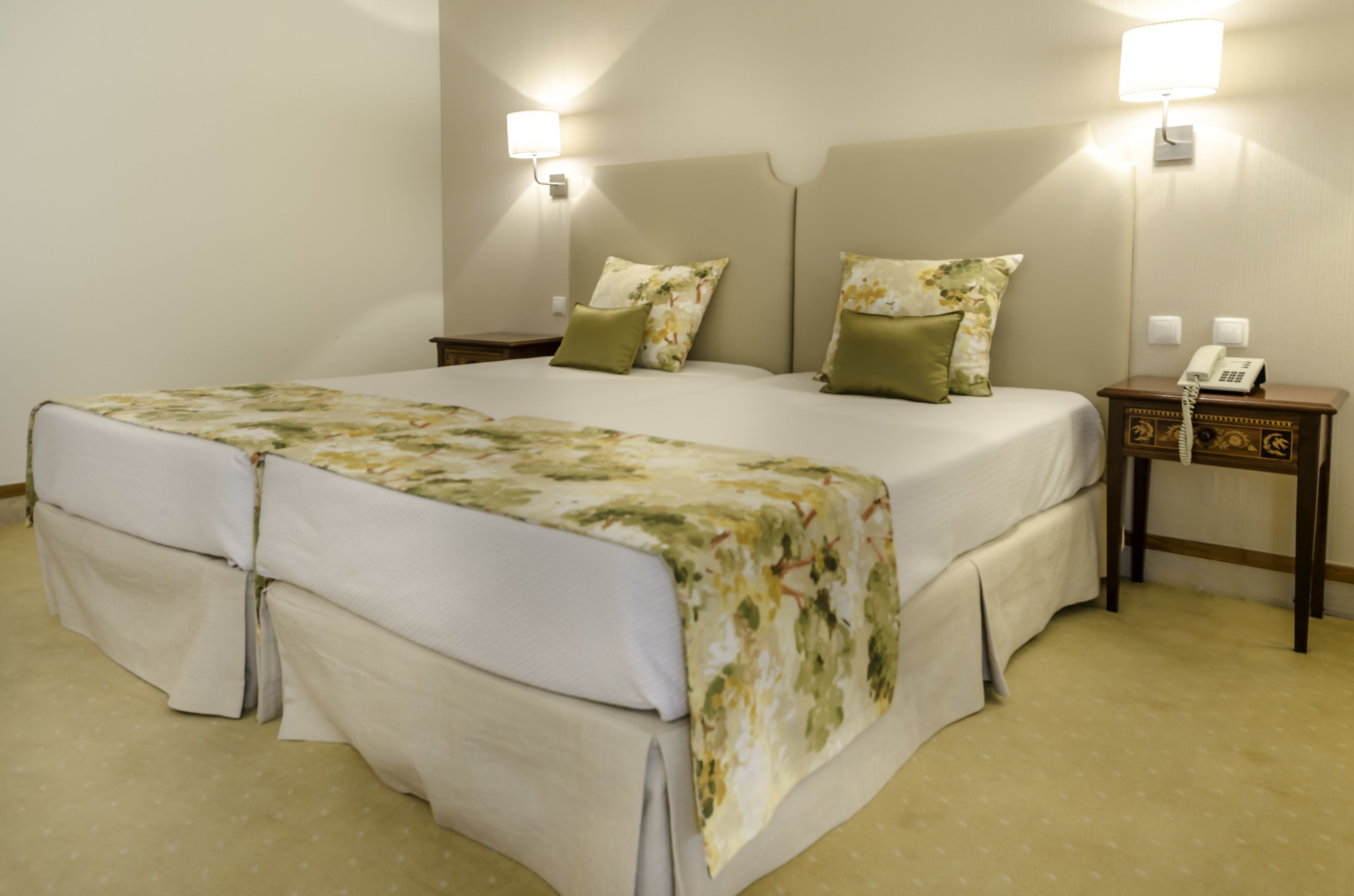 Una cama doble con ropa de cama floral, dos mesitas de noche con lámparas y un teléfono al lado derecho.