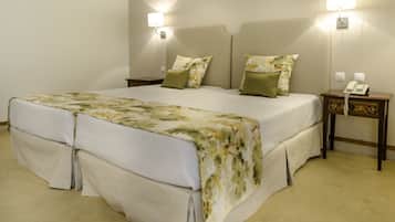Una cama doble con ropa de cama floral, dos mesitas de noche con lámparas y un teléfono al lado derecho.
