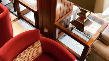 Uma poltrona vermelha com uma almofada estampada, uma mesinha de madeira com abajur e uma mesa de centro com tampo de vidro.