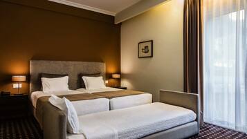 Une chambre d’hôtel avec un grand lit, deux tables de chevet, une chaise et une fenêtre avec des rideaux.