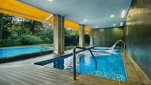 A modern indoor pool area with a clear view of the surrounding greenery, a separate hot tub, and a wooden deck.