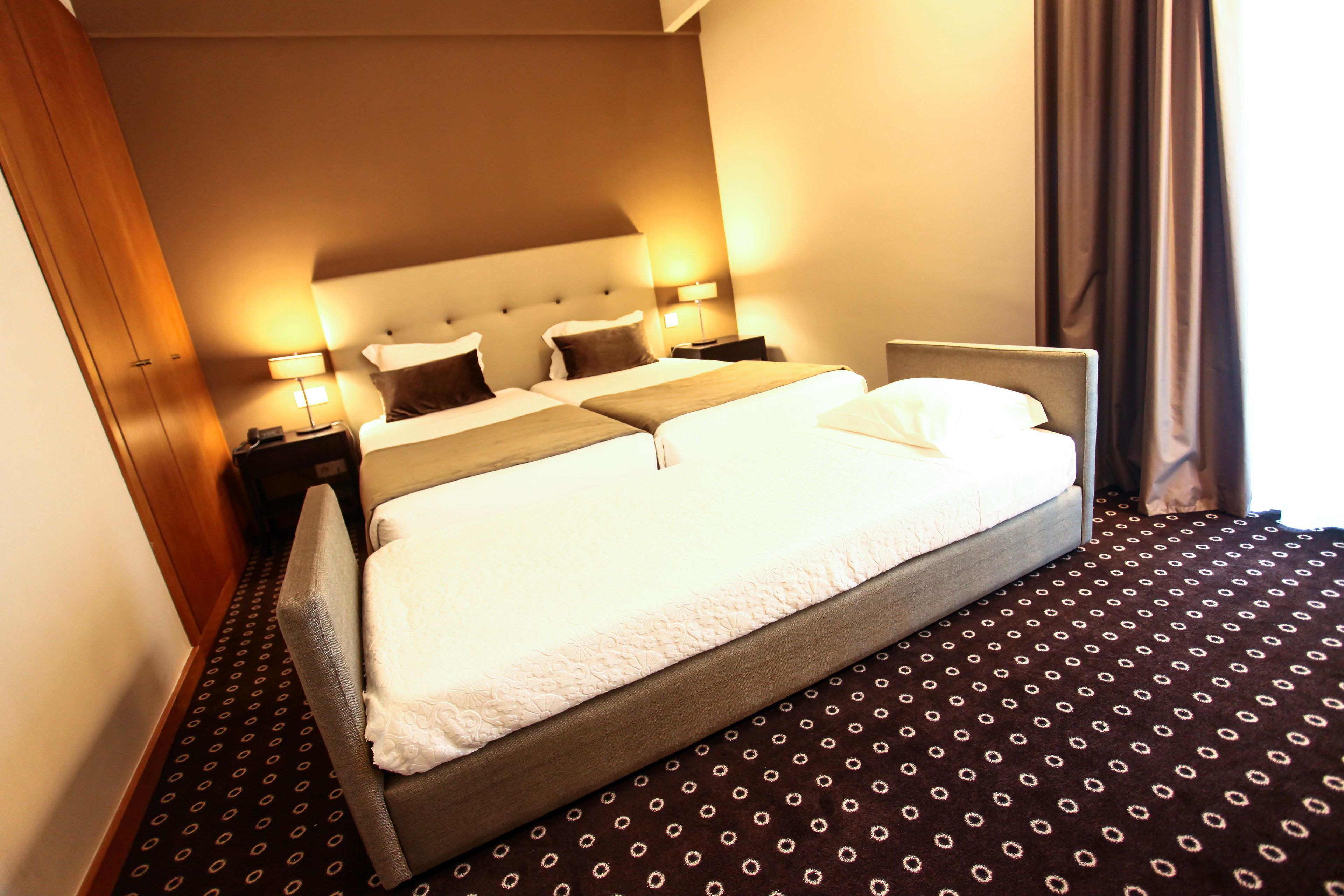 A hotel room with a large bed, two bedside tables, a headboard, and a patterned carpet.