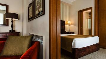 A hotel room with a bed, a red armchair, a nightstand with a lamp, and framed pictures on the wall.