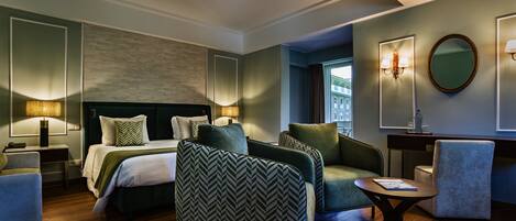 Ein modernes Hotelzimmer mit einem großen Bett, zwei Sesseln, einem kleinen Tisch und einem Schreibtisch.