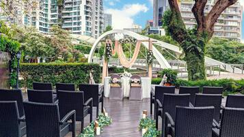 An outdoor wedding venue with wicker chairs and a white archway.