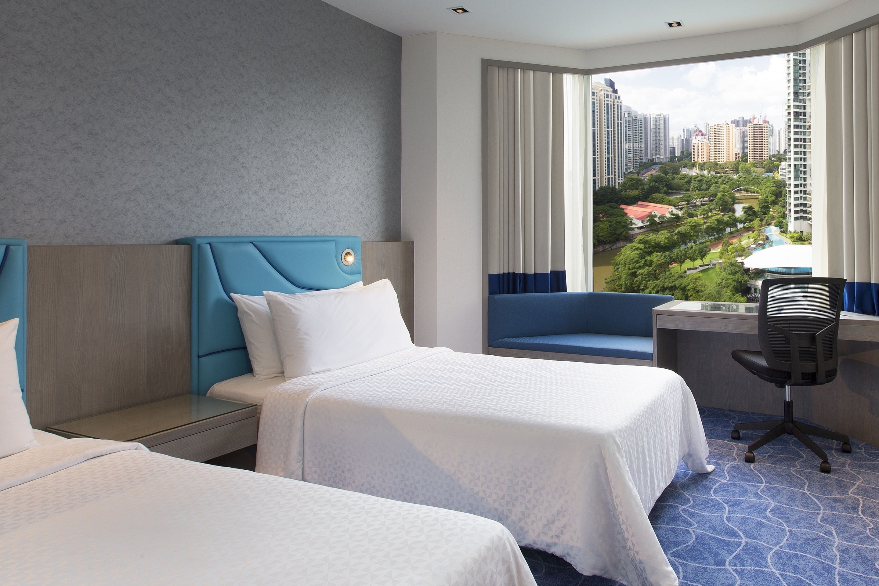 A hotel room with two beds, a desk, and a view of a cityscape.