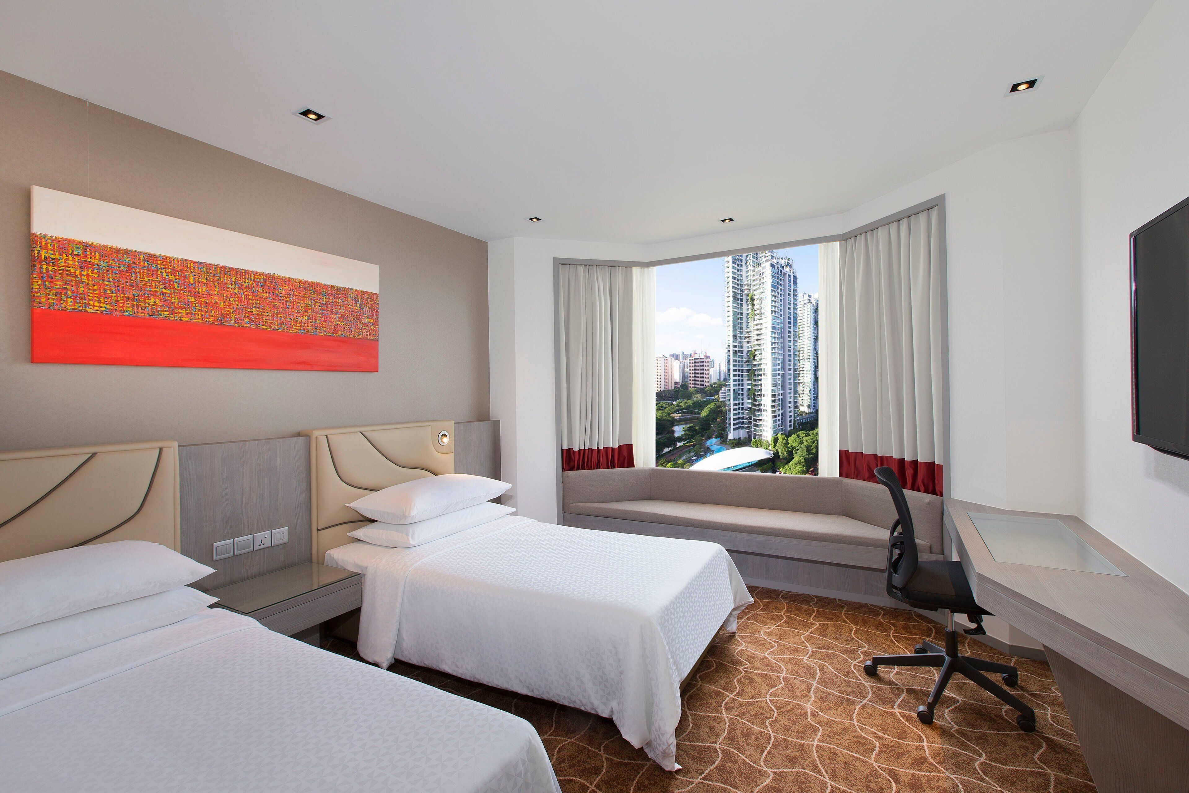 A hotel room with two beds, a desk, a chair, a large window with curtains, and a city view.